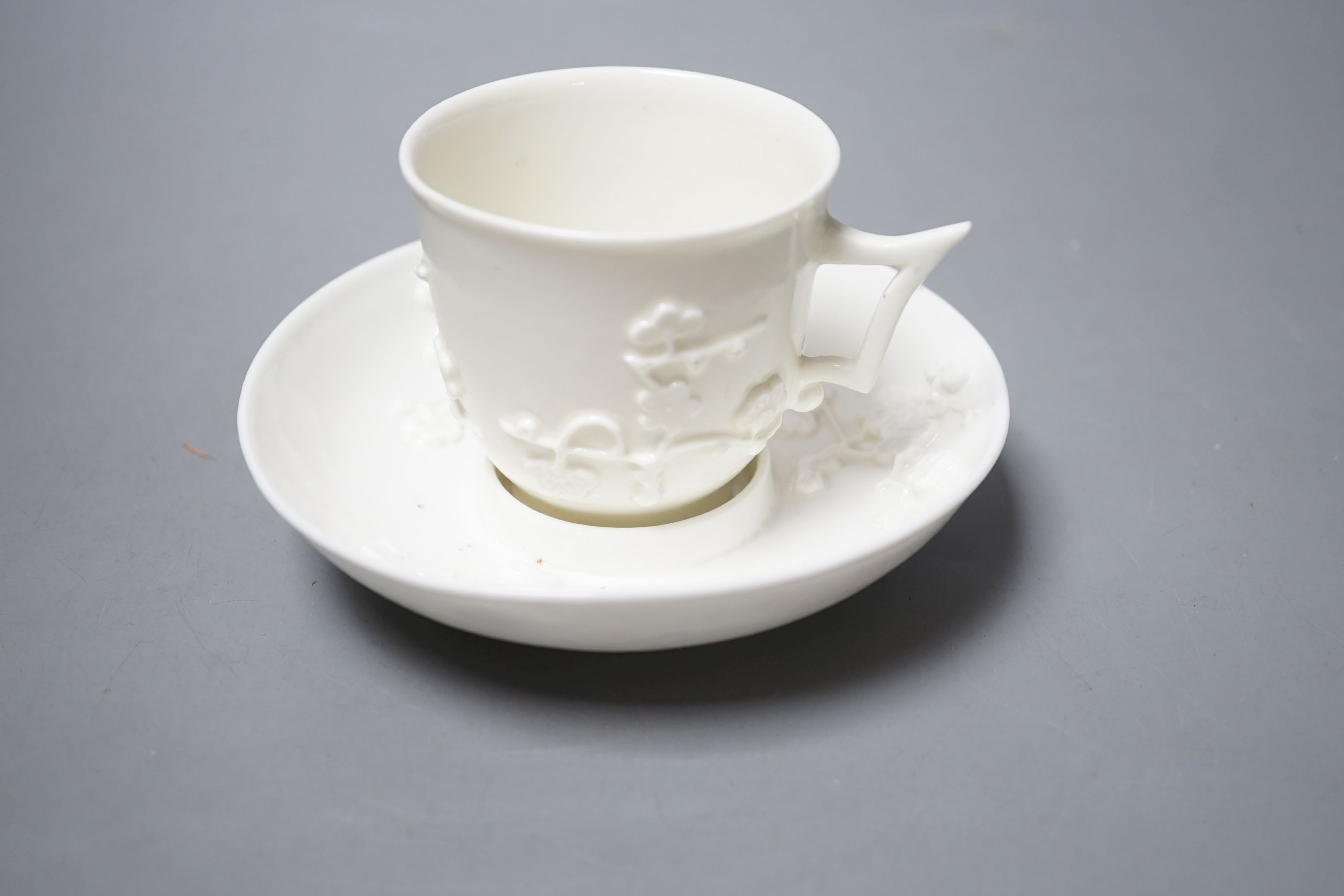 A St Cloud white-glazed coffee cup with angular handle and scroll terminal and matching trembleuse saucer applied with sprigs of flowering prunus c. 1730